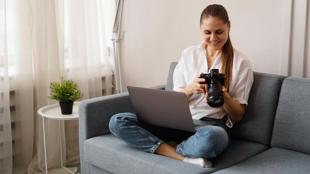 Happy young woman with photo camera using laptop at home. The photographer looks at the pictures taken and sits on the couch.