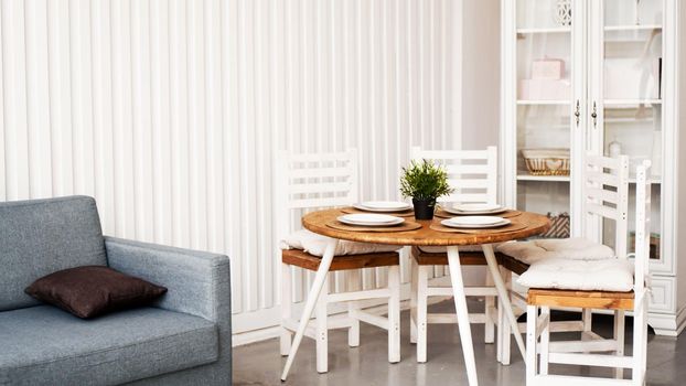 Round wooden dining table and white chairs. Modern Scandinavian interior in the kitchen and dining room.