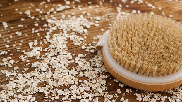 Wooden round massage brush on a wooden background. Scattered oatmeal. The concept of cosmetics for body from natural ingredients