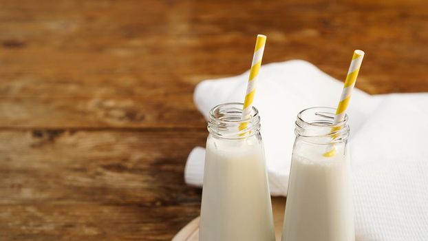 Two bottles of organic rustic milk on wooden table with yellow paper straws. Copy space