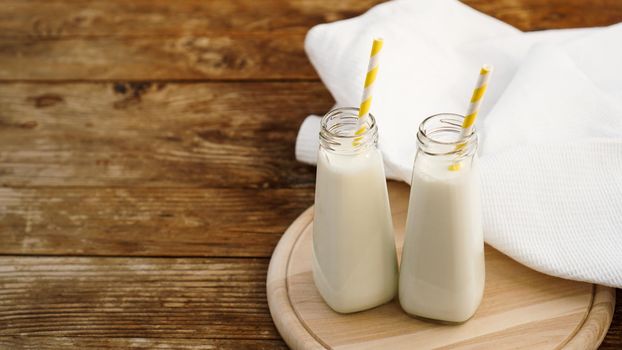 Two bottles of organic rustic milk on wooden table with yellow paper straws. Copy space