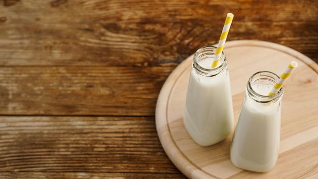 Two bottles of organic rustic milk on wooden table with yellow paper straws. Copy space