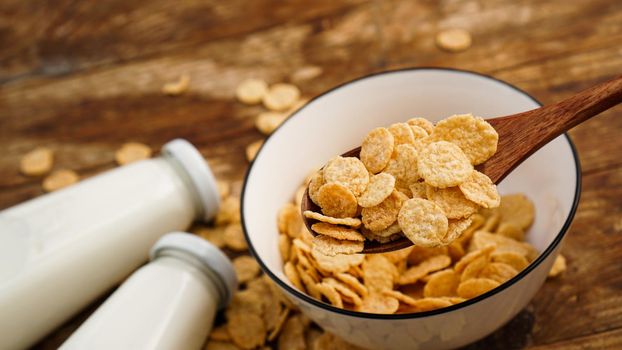 Healthy cornflakes and milk and a wooden spoon on wooden table. Glass bottles with milk for a healthy breakfast