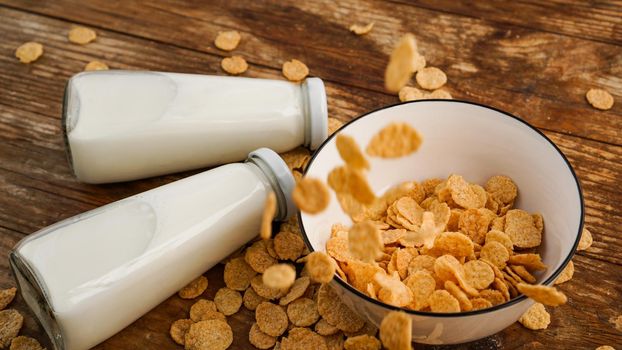 Healthy eating background. Dry flakes fall into a bowl and two bottles of milk. Wood background