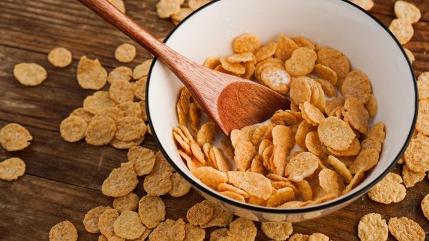 Yellow cornflakes in a white bowl. Wooden spoon in a bowl. The concept of healthy eating and delicious breakfast. Wood background