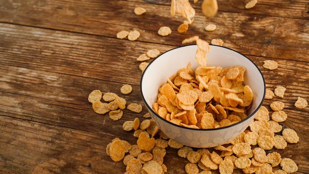 Cereals falling in a white bowl on a wooden table. Bright photo. Healthy quick breakfast