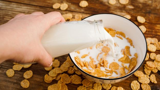 Healthy eating background. Pouring in fresh milk into bowl of cornflakes. Wood background