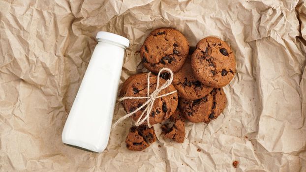 Cookies with chocolate drops on craft paper and bottle of milk. Natural handmade organic snakes for healthy breakfast