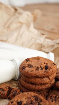 Cookies with chocolate drops on craft paper and bottles of milk. Natural handmade organic snakes for healthy breakfast. Vertical photo
