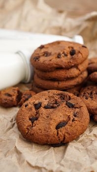 Cookies with chocolate drops on craft paper and bottles of milk. Natural handmade organic snakes for healthy breakfast. Vertical photo