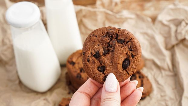 Female hands holding chocolate chip cookies. Selective focus. Cookies with milk on craft paper