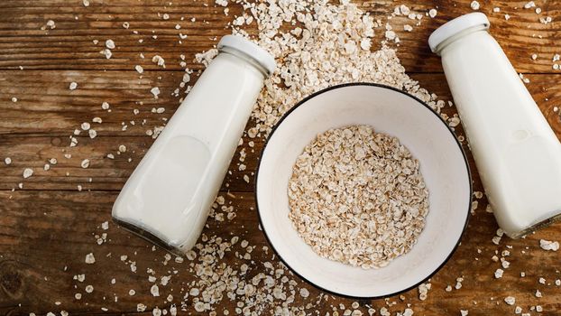 Oat flakes in white bowl and bottles of fresh milk. Wooden rustic background