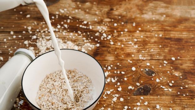 Oatmeal in a bowl. Milk is pouring into a bowl on a wooden background. Healthy breakfast