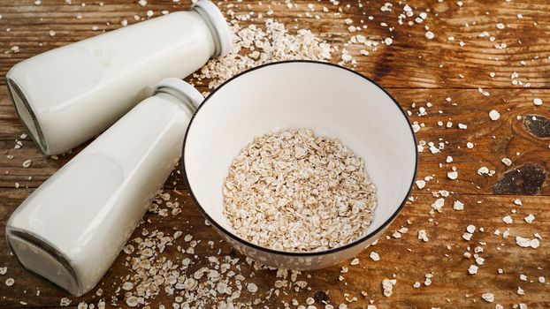 Oat flakes in white bowl and bottles of fresh milk. Wooden rustic background