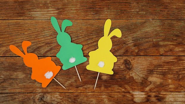 Easter hand-made. Handmade decor for the holiday. Colored paper rabbits are attached to toothpicks on wooden background. Can be used to decorate Easter cupcakes