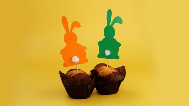 Muffin decorated with a paper rabbit on a toothpick. Easter decor for cupcakes. Festive sweets and pastries. Yellow background