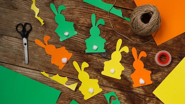 Easter bunnies made of paper on a wooden background. Create a decor for easter. Scissors and a skein of rope. DIY Easter garland making