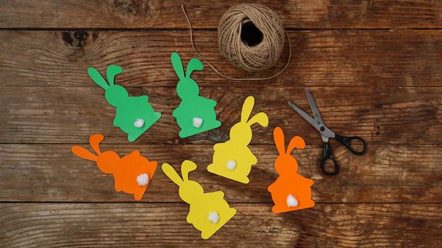 Easter bunnies made of paper on a wooden background. Create a decor for easter. Scissors and a skein of rope. DIY Easter garland making