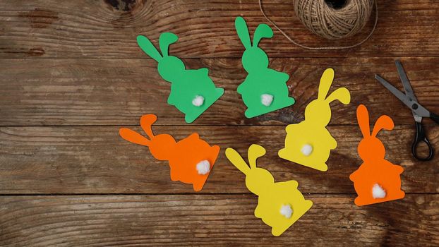 Easter bunnies made of paper on a wooden background. Create a decor for easter. Scissors and a skein of rope. DIY Easter garland making