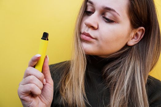 Close up of a young girl smokes a disposable electronic cigarette. Bright yellow background. Alternative to regular cigarettes and vape