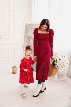 Mom and little daughter in red dresses in a bright bedroom in a Scandinavian style. Happy family. Mom holds a bouquet of daisies - spring photo