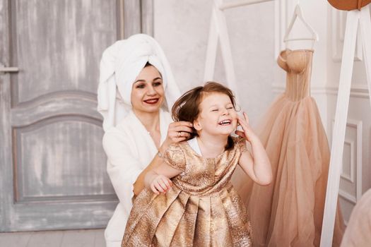 Happy mother and daughter are putting on a dress. The mother is wearing a white bathrobe. They are going to the party. Daughter laughs