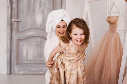 Happy mother and daughter are putting on a dress. The mother is wearing a white bathrobe. They are going to the party. Daughter laughs