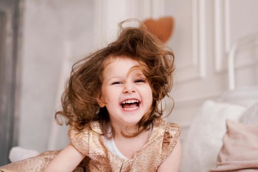 Portrait of a happy three-year-old girl. The blonde-haired child laughs. She is dressed in a beautiful beige dress for a children's party.