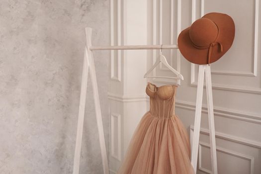 Beige dress and hat on a hanger. White Scandinavian wardrobe style