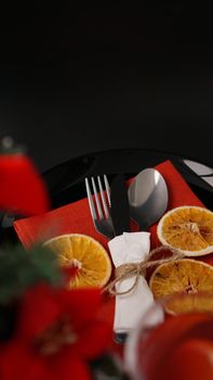 Setting for festive Christmas dinner on black table with New year decoration and dry oranges