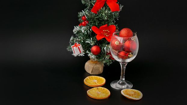 New Year tree on a black background. Red Christmas balls in a wine glass, decor from dry oranges