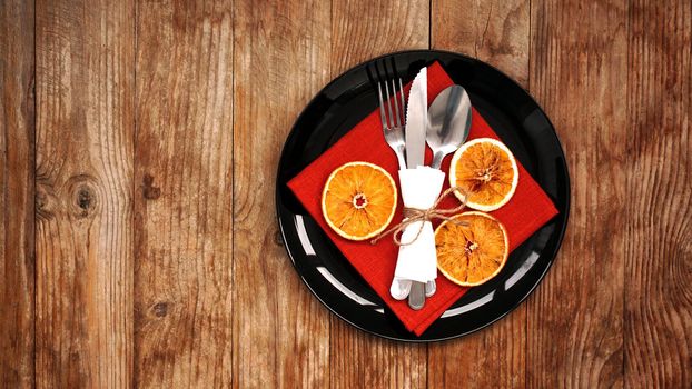 Christmas dinner decoration with dried oranges and a red napkin on a black plate on wooden background. Space for text