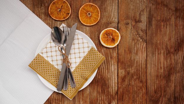Overhead view of fall Thanksgiving or Christmas table setting over wooden table with copy space. White plate with dry oranges
