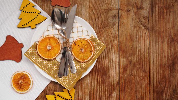 Overhead view of Christmas table setting over wooden table with copy space. White plate with dry oranges and wooden christmas figurines