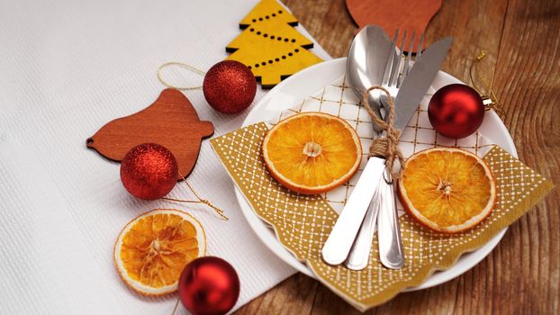 Overhead view of Christmas table setting over wooden table with copy space. White plate with dry oranges, red balls and wooden christmas figurines