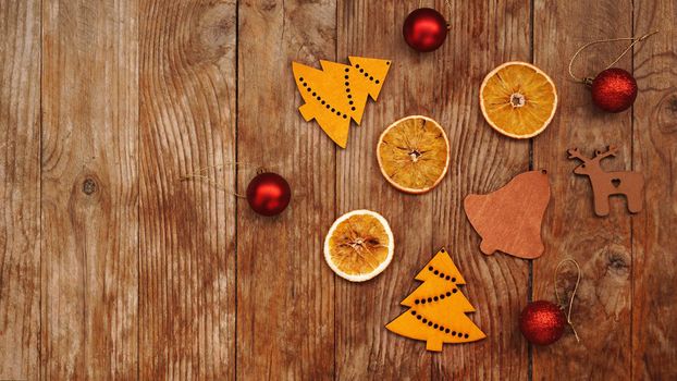 Dry oranges, red balls and wooden christmas figurines on rustic brown wooden background with place for text