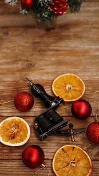 Tattoo machines on a christmas background - christmas decor with red balls and dried oranges on a wooden background. Vertical photo