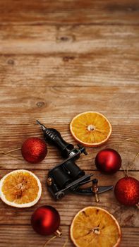 Tattoo machines on a christmas background - christmas decor with red balls and dried oranges on a wooden background. Vertical photo