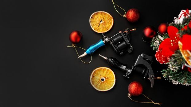 Tattoo machines on a christmas background - christmas decor with tree on a blsck background