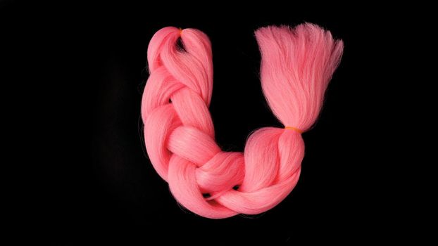 Pink kanekalon hangs on a black background