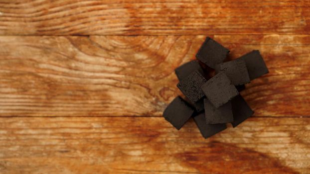 Cubes of coconut coal for hookah on wooden background. Place for text