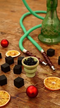 Hookah background for new year and christmas. Hookah, charcoal, dry orange slices and Christmas red balls on a wooden background. Vertical photo