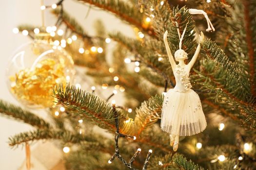 Beautiful ballerina decorates a Christmas tree branch. Festive background of a green Christmas tree and gold balls