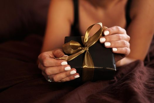 The woman opens a gift in a black box with a gold ribbon. Closeup photo