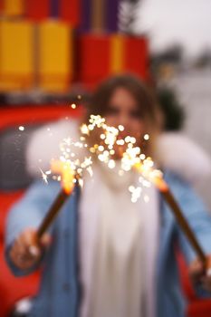 Female hands are holding burning sparklers. Woman outdoors in winter. Blurred background