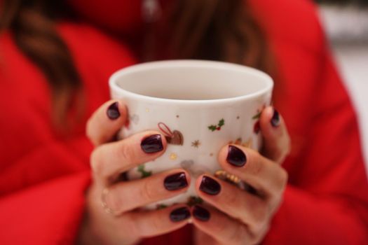 Female hands holding christmas cup with hot dark drink outside on winter day