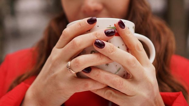 Female hands holding christmas cup with hot dark drink outside on winter day