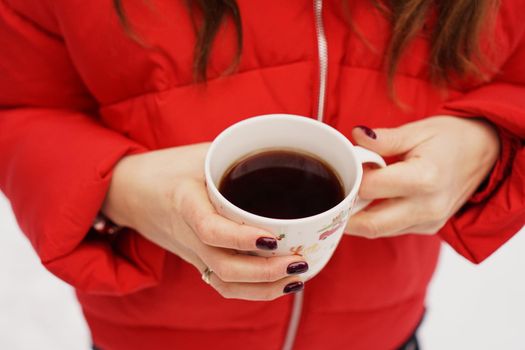 Female hands holding christmas cup with hot dark drink outside on winter day