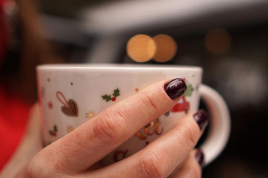 Female hands holding christmas cup with hot dark drink outside on winter day