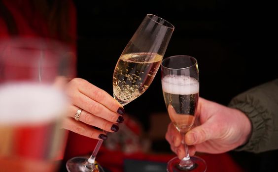 Dating concept - close up of champagne glasses in male and female hands - Outside